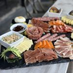 A large charcuterie board with assorted meats, cheeses, fruits, nuts, and dips artfully arranged 